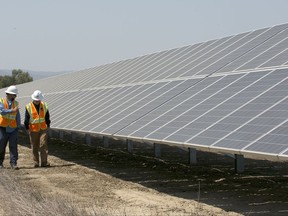 FILE - In this Aug. 17, 2017, file photo, solar tech Joshua Valdez, left, and senior plant managerTim Wisdom walk past solar panels at a Pacific Gas and Electric Solar Plant, in Dixon, Calif. Cheap solar panels imported from China and other countries have led to a boom in the U.S. solar industry, where rooftop and other installations have surged 10-fold since 2011. But two U.S. solar manufacturing companies say the flood of imports has led one to bankruptcy and forced the other to lay off three-quarters of its workforce. (AP Photo/Rich Pedroncelli, File)