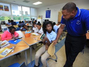 In this Aug. 29, 2017, photo, Turner Elementary School Principal Eric Bethel, right, talks to fifth grade student Kierra Porter, during her reading class, at Turner Elementary School in southeast Washington. Most of the states that first endorsed the Common Core academic standards are still using them in some form, despite continued debate over whether they are improving student performance in reading and math. Bethel says the new guidelines push students to learn "not only the how, but also the why behind the mathematics. Students are learning more and what's expected of them is much more rigorous than before," Bethel said.  (AP Photo/Manuel Balce Ceneta)