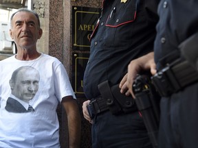 A man wearing a shirt showing a picture of Russian President Vladimir Putin stands by Montenegro police officers guarding the entrance to the court building during the trial in Podgorica, Montenegro, Wednesday, Sept. 6, 2017. The trial has opened of 14 alleged coup plotters, including two Russians, suspected of a foiled bid to overthrow the Montenegrin government to thwart the Balkan country's NATO bid. (AP Photo/Risto Bozovic)