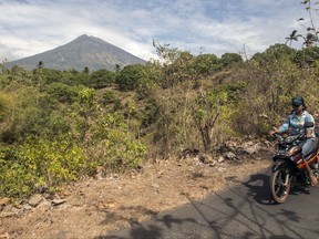 A villager rides past by with Mount Agung seen in the background in Karangasem, Bali, Indonesia, Sunday, Sept. 24, 2017. Thousands of villagers on the Indonesian resort island have been evacuated to temporary shelters amid fear that Mount Agung will erupt for the first time in more than half a century. Its last eruption in 1963 killed 1,100 people. (AP Photo/J.P. Christo)