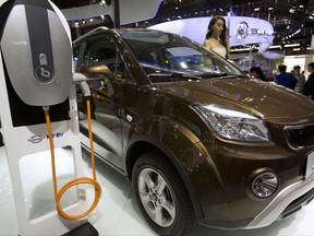 FILE - In this April 26, 2016, file photo, a staff member stands next to an e.Cool electric SUV by Chinese automaker Changjiang on display at the Beijing International Automotive Exhibition in Beijing. China has stepped up pressure on automakers to accelerate development of electric cars by raising the first-year target for a planned system of production quotas but delayed its rollout until 2019. (AP Photo/Mark Schiefelbein, File)