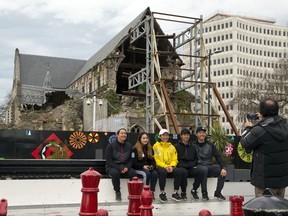 In this Sept. 5, 2017 photo, tourists pose for a photo near the Feb. 22, 2011 earthquake damaged ChristChurch Cathedral in Christchurch, New Zealand. For more than six years since a deadly earthquake struck Christchurch, the city's iconic cathedral has sat in ruins in the city center. For many locals, the wreck has become a visual reminder of the infighting that has slowed the city's broader rebuild. (AP Photo/Mark Baker)
