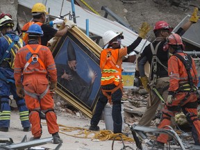 Search and rescue workers remove a painting from a felled office building brought down by a 7.1-magnitude earthquake, as others raise their arms as a sign for people to maintain silence during their search for survivors in the Roma Norte neighborhood of Mexico City, Saturday, Sept. 23, 2017. As rescue operations stretched into day 5, residents throughout the capital have held out hope that dozens still missing might be found alive. (AP Photo/Moises Castillo)