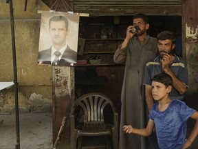 People stand near a portrait of Syrian President Bashar al-Asad in a street in the city of Deir ez-Zor, Syria, Friday, Sept. 15, 2017. (AP Photo)