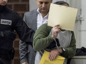 One of four defendants is guided by police  in the higher regional court in Stuttgart, Germany, Monday, Sept. 25 2017.   Four asylum-seekers have gone on trial in Germany accused of executing 36 members of the Syrian security forces while they were members of the Nusra Front extremist group. Prosecutors say the four men killed their victims - police officers, security officials and soldiers - at a garbage site in the Syrian city of Tabqa in March 2013. The defendants appeared before Stuttgart's regional court Monday on charges of war crimes, murder and membership in a foreign terrorist organization.  (Sebastian Gollnow/dpa via AP)