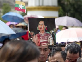 A supporter holds the portrait of Myanmar's State Counsellor Aung San Suu Kyi and Myanmar national flag as he watches live broadcasting of a televised speech to the nation by Suu Kyi, Tuesday, Sept. 19, 2017, in Yangon, Myanmar.  Suu Kyi is defending her country against international criticism over a mass exodus of Rohingya Muslims by saying most of their villages remain intact, and that it's important to understand why conflict did not break out everywhere. (AP Photo/Thein Zaw)