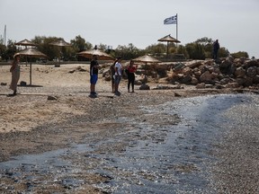 People stand on a beach where an oil spillage has been washed-up at Glyfada suburb, near Athens, on Thursday,Sept. 14, 2017. Greek authorities insist they are doing everything they can to clean up pollution caused by an oil spill following the sinking of a small oil tanker that has left large sections of the Greek capital's coastal areas coated in viscous, foul-smelling oil. (AP Photo/Yorgos Karahalis)