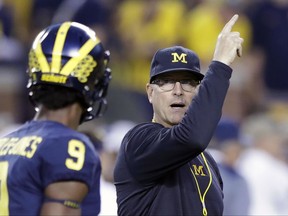 Michigan head coach Jim Harbaugh, right, signals to his team during warmups for an NCAA college football game against Michigan State, Saturday, Oct. 7, 2017, in Ann Arbor, Mich. (AP Photo/Carlos Osorio)