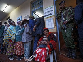 An elderly Kenyan woman takes a rest after casting her vote, while a Kenyan policeman provides secrurity, just after dawn in President Uhuru Kenyatta's hometown of Gatundu, Kenya Thursday, Oct. 26, 2017. Kenya is holding its second presidential election since August despite high tension and the main opposition leader's call for his followers to boycott. (AP Photo/Ben Curtis)