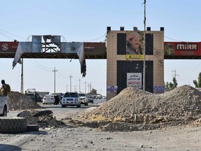 A picture taken on October 20, 2017 shows cars carrying fighters loyal to the federal goverment passing en route to the multi-ethnic northern Iraqi city of Kirkuk, beneath banners supporting a "Yes" vote for the September Kurdish Independence referendum and a poster of Iraq's Kurdistan region president Massud Barzani. Iraqi forces clashed with Kurdish peshmerga fighters on October 20 and retook control of the last sector of the disputed province of Kirkuk, with a general killed in the fighting, security sources said.