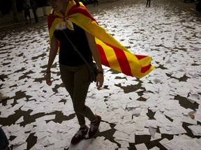 A woman wearing an estelada or independence flag walks a long a street covered with referendum ballots threw by pro-independence demonstrators, during a rally in front of the Spanish Partido Popular ruling party headquarters in Barcelona, Spain, Tuesday Oct. 3, 2017