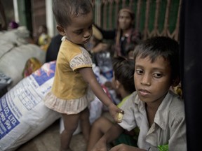 In this Oct. 2, 2017, file photo, two-year old Noyem Fatima offers a piece of banana to her elder brother Yosar Hossein, 7, as they sit on a sidewalk with their belongings in Leda, Bangladesh. Hossein carried his baby sister Noyem for seven days fleeing from their village in Myanmar to a refugee camp in Bangladesh with their mother and other siblings. (AP Photo/Gemunu Amarasinghe, File)