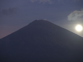 A full moon is set behind the Mount Agung volcano in Karangasem, Bali, Indonesia, Friday, Oct. 6, 2017. More than 140,000 people have fled from the surrounds of Mount Agung since authorities raised the volcano's alert status to the highest level on Sept. 22 after a sudden increase in tremors. It last erupted in 1963, killing more than 1,000 people. (AP Photo/Firdia Lisnawati)