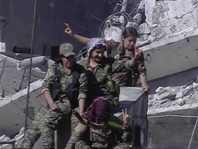 This frame grab from a video released on Thursday, Oct. 19, 2017 provided by Ronahi TV, a Kurdish TV channel media outlet that is consistent with independent AP reporting, shows members of a Kurdish female militia, the Women's Protection Units, flashing victory signs as they celebrate the victory against the Islamic State group, in Raqqa, Syria. The militia that took part in freeing the northern Syrian city of Raqqa from the Islamic State group said it will continue the fight to liberate women living under the extremist group's brutal rule. (Ronahi TV, via AP)