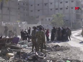 This frame grab from a video provided on Friday, Oct. 13, 2017 by Turkey-based Kurdish Mezopotamya agency media outlet that is consistent with independent AP reporting, shows U.S.-backed Syrian Democratic Forces (SDF) fighters, stand around Syrian civilians who fled from the areas that still controlled by the Islamic State militants, in Raqqa, Syria. Scores of civilians including women and children are fleeing the last few remaining neighborhoods held by the Islamic State group in Syria's northern city of Raqqa, ahead of an anticipated final push by U.S.-backed fighters seeking to liberate the city. (Mezopotamya Agency, via AP)