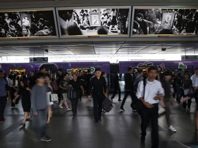 In this Monday, Oct. 16, 2017, photo, Skytrain passengers dressed primarily in black come and go under black and white images in memory of the late King of Thailand at a station platform in Bangkok, Thailand. The muted colors of mourning have settled over Bangkok once again in recent weeks as the country marks a year since the death of its beloved monarch, King Bhumibol Adulyadej, and prepares for the national spectacle of his cremation next week. (AP Photo/Wally Santana)