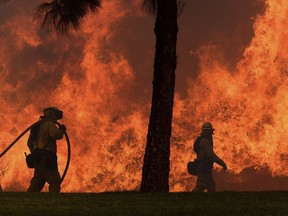 FILE--In this Oct. 9, 2017, file photo, firefighters battle flames along Jamboree Road in Orange, Calif. The long and brutal 2017 wildfire season is stressing the state and federal agencies that have to pay for the army of ground crews and machinery required to fight them. (Will Lester/The Orange County Register via AP, file)