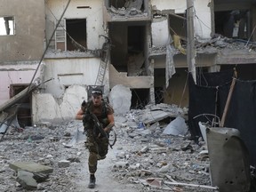 FILE - In this July 27, 2017 file photo, A U.S.-backed Syrian Democratic Forces fighter runs in front of a damaged building as he crosses a street on the front line, in Raqqa, Syria. (AP Photo/Hussein Malla, File)