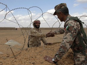 FILE - In this Tuesday, Feb. 14, 2017 file photo, a member of the Syrian Tribes Army, left, that guards the Syrian side of the berm on the north eastern border with Jordan, shakes hands with a Jordanian soldier. Jordan hopes a cease-fire it helped negotiate in neighboring southern Syria will eventually lead to a secure border, the reopening of a vital trade crossing and a gradual return home for Syrian war refugees who sought asylum in the kingdom _ but for now, however, these goals seem out of reach. (AP Photo/ Raad Adayleh, File)