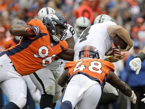 Oakland Raiders quarterback Derek Carr (4) is tackled by Denver Broncos defensive end Shelby Harris, left, and outside linebacker Shaquil Barrett during the second half of an NFL football game Sunday, Oct. 1, 2017, in Denver. Carr was juried on the play. (AP Photo/Joe Mahoney)
