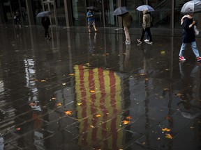 People walk past a Catalan flag reflected on the ground in Barcelona, Spain, Thursday, Oct. 19, 2017. Spain's government on Thursday immediately rejected a threat by Catalonia's leader to declare independence unless talks are held, calling a special Cabinet session for the weekend to activate measures to take control of the region's semi-autonomous powers. (AP Photo/Emilio Morenatti)