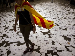 FILE, In this Sunday, Oct. 1, 2017 file photo, a woman wearing an estelada or independence flag walks a long a street covered with referendum ballots thrown by pro-independence demonstrators, during a rally in front of the Spanish Partido Popular ruling party headquarters in Barcelona, Spain. The ballot boxes arrived from France in the dead of night, were stored in homes and improvised hidey-holes, and then secretly shuttled to polling stations across Catalonia right under the nose of police. (AP Photo/Emilio Morenatti, File)