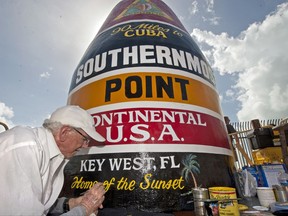 In this photo provided by the Florida Keys News Bureau, artist Danny Acosta completes lettering the Southernmost Point in the Continental U.S.A. marker Monday, Oct. 23, 2017, in Key West, Fla. One of the most-photographed tourism icons in the Florida Keys was pummeled by Hurricane Irma on Sept. 10, stripping most of the paint and a large chunk of stucco. (Rob O'Neal/Florida Keys News Bureau via AP)