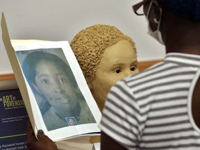 In this Oct. 21, 2016 photo, Sheila Williams holds up a faded, photocopied picture of a woman near a sculpture of an unidentified 1985 female murder victim during a forensic conference in Tampa, Fla.