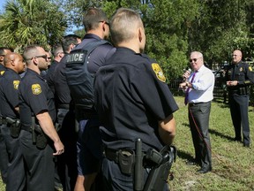 In this Wednesday, Oct. 25, 2017 photo, Mayor Bob Buckhorn, center right, addresses members of the Tampa Police Department while Interim Police Chief Brian Dugan, right, looks on during a roll call and press conference at Giddens Park in the Seminole Heights neighborhood in Tampa, Fla. Buckhorn told police officers looking for a suspect in three fatal and apparently random shootings in the neighborhood to hunt him down and "bring his head to me."  (Gabriella Angotti-Jones/Tampa Bay Times via AP)