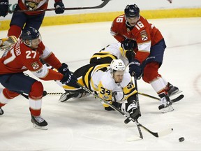 Pittsburgh Penguins right wing Tom Kuhnhackl (34) reaches for the puck with Florida Panthers' Nick Bjugstad (27) and Aleksander Barkov (16) during the first period of an NHL hockey game, Friday, Oct. 20, 2017 in Sunrise, Fla. (AP Photo/Wilfredo Lee)