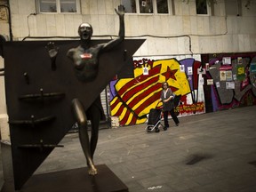 A woman pushes a trolley past a graffiti of an "estelada", or Catalonia independence flag, at the Gracia neighborhood in Barcelona, Wednesday, Oct. 4, 2017. Catalonia's regional government is mulling when to declare the region's independence from Spain in the wake of a disputed referendum that has triggered Spain's most serious national crisis in decades. (AP Photo/Francisco Seco)