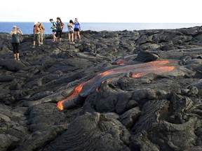 FILE - In this Monday, Aug. 8, 2016 file photo, visitors look at lava from Kilauea, an active volcano on Hawaii's Big Island, as it flows toward the ocean in Hawaii Volcanoes National Park near Kalapana, Hawaii. Hawaii residents and an organization representing federal workers filed a lawsuit against the Federal Aviation Administration on Wednesday, Oct. 4, 2017 seeking to force it to do something about tour helicopters buzzing their communities and national parks across the country.  (AP Photo/Caleb Jones, File)
