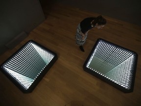 A staff member poses for photographs looking at Chilean-born artist Ivan Navarro's two light box and mirror installation "The Twin Towers" during the media preview for the "Age of Terror: Art since 9/11" exhibition at the Imperial War Museum in London, Wednesday, Oct. 25, 2017.  The exhibition, which runs from Oct. 26 until May 28, 2018, considers artists' responses to war and conflict since the attacks of Sept. 11, 2001. (AP Photo/Matt Dunham)