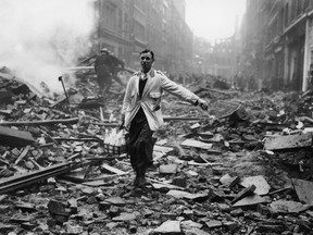 A milkman walks through a London street devastated during a German bombing raid.