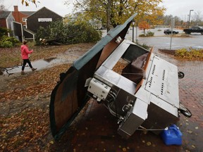 A woman walks by a food stand and a tree that were toppled by a storm in Freeport, Maine, Monday, Oct. 30, 2017. A strong wind storm has caused widespread power outages. (AP Photo/Robert F. Bukaty)