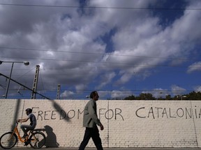 People pass in front of graffiti reading "Freedom for Catalonia" in Barcelona, Spain, Monday, Oct. 23, 2017. Catalonia's regional parliament will hold a debate this week on Spain's plan to take direct control of the northeastern region -- a session many fear could become a cover for a vote on declaring independence. (AP Photo/Manu Fernandez)