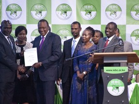 In this Aug. 11, 2017, photo, Kenyan electoral official Roselyn Akombe, center right, stands as President Uhuru Kenyatta, third from left, receives his electoral win certificate, later nullified, from Chairman of the Electoral Commission Wafula Chebukati, left, as Deputy President William Ruto, right, looks on at the results center in Nairobi, Kenya. Akombe resigned Wednesday, Oct. 18, 2017 in a statement from New York saying the rerun of the presidential election scheduled for Oct. 26 cannot be free and fair. (AP Photo/Sayyid Abdul Azim)