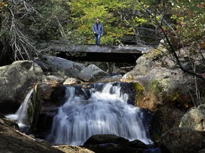 In this Thursday, Sept. 28, 2017 photo a hiker walks out on a bridge to view a waterfall at the Crystal Cascades in Pinkham Notch, N.H. Despite forecasts for brilliant foliage throughout the Northeast this year, long-time leaf watchers say the leaves this fall are dull and weeks behind schedule in their turn from green to the brilliant hues of autumn. (AP Photo/Robert F. Bukaty)