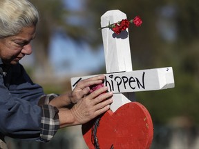 Nancy Hardy, of Las Vegas, touches a flower on a cross placed in honor of mass shooting victim John Phippen, of Santa Clarita, Calif., Friday, Oct. 6, 2017, in Las Vegas. A gunman opened fire on an outdoor music concert on Sunday killing dozens and injuring hundreds.(AP Photo/Gregory Bull)