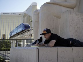 Las Vegas resident Todd Hessler writes in his notebook while sitting on a statue at the Luxor with Mandalay Bay resort and casino in the background on Wednesday, Oct. 4, 2017, in Las Vegas. A gunman opened fire on an outdoor music concert on Sunday killing dozens and injuring hundreds. (AP Photo/John Locher)