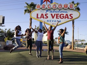 In this Tuesday, Oct. 3, 2017 photo, tourists pose for photos in front of the Welcome to Las Vegas sign that has flowers honoring the people who died in a mass shooting on Sunday in Las Vegas. But even though the city is in mourning, for many it is business as usual with celebrations and parties continuing. (AP Photo/Chris Carlson)