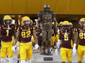FILE - In this Aug. 31, 2017, file photo, players file past the Pat Tillman statue, with one reaching to touch it, at an NCAA college football game between Arizona State and New Mexico State in Tempe, Ariz. Ever since Arizona State unveiled a statute of former defensive back Pat Tillman outside the school's student-athlete facility just before the season, the Sun Devils have made a point of touching the statue as they head to the field before every home game. (AP Photo/Rick Scuteri, File)