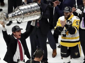 FILE - In this June 11, 2017, file photo, Pittsburgh Penguins head coach Mike Sullivan hoists the Stanley Cup as Bryan Rust (17) watches after defeating the Nashville Predators 2-0 in Game 6 of the NHL hockey Stanley Cup Final in Nashville, Tenn. Coach Sullivan challenged his players to three-peat even while they were still partying after a second straight title. The Penguins think they can do it, something Wayne Gretzky, Mario Lemieux and Steve Yzerman could not.  (AP Photo/Jeff Roberson, File)