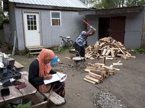 In this Sept. 7, 2017 photo, a girl studies for school while a man chops wood in the Muslim enclave of Islamberg in Tompkins, N.Y. Followers of Pakistani cleric Sheikh Mubarik Gilani settled Islamberg in the 1980s, fleeing crime and crowding in New York City. The mostly African-American settlers wanted a better place to raise their children. (AP Photo/Mark Lennihan)