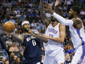 New Orleans Pelicans forward DeMarcus Cousins (0) passes in front of Oklahoma City Thunder center Steven Adams (12) and forward Paul George, right, during the first quarter of an NBA preseason basketball game in Oklahoma City, Friday, Oct. 6, 2017. (AP Photo/Sue Ogrocki)