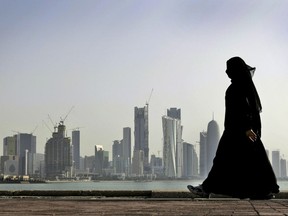 FILE- In this May 14, 2010 file photo, a Qatari woman walks in front of the city skyline in Doha, Qatar. The U.S. military says it has halted some military exercises with Gulf countries over the ongoing diplomatic dispute targeting Qatar. (AP Photo/Kamran Jebreili, File)