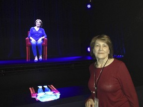 In this Oct. 20, 2017 photo, Holocaust survivor Fritzie Fritzshall poses for a portrait in front of her 3D hologram at the Illinois Holocaust Museum in Skokie, Ill. Fritzshall is one of 13 Holocaust survivors who tell their stories through holographic images that invite the audience to ask questions, creating what feels like a live conversation. The exhibit in Skokie marks the first time that the voice-recognition technology powering conversations with audiences has been married to 3-D holographic technology to tell survivors' stories. (AP Photo/Don Babwin)