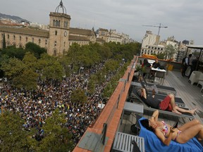Tourists from Switzerland sunbathe at a terrace overlooking Universitat square as demonstrators gather in protest in downtown Barcelona, Spain, Tuesday Oct. 3, 2017