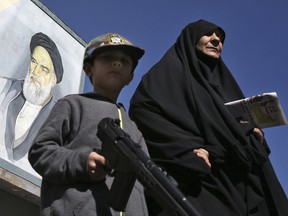 An Iranian woman and a boy with a toy gun walk past a mural of the late revolutionary founder Ayatollah Khomeini in downtown Tehran, Iran, Friday, Oct. 13, 2017. (AP Photo/Vahid Salemi)
