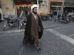 In this Sunday, Oct. 8, 2017 photo, a clergyman crosses a street in downtown Tehran, Iran. As U.S. President Donald Trump threatens the Iran nuclear deal, those living in Tehran feel that an accord they have yet to benefit from may already be doomed, hardening their skepticism about America. Trump is set to deliver a speech on Iran this week in which he is expected to decline to certify Iran's compliance in the landmark 2015 agreement. (AP Photo/Vahid Salemi)